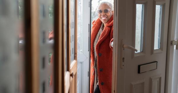 A lady looks into her house through her open front door. She is smiling.