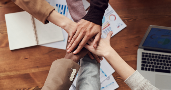 Decorative stock image of six people putting their hands in for a group celebration over a desk
