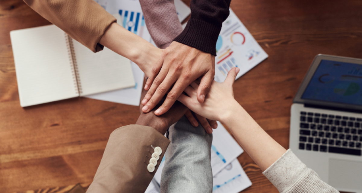 Decorative stock image of six people putting their hands in for a group celebration over a desk